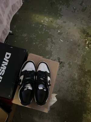 Nike Dunk Low svart/vit sneakers - Säljer ett par Nike Dunk Low sneakers i svart och vitt. Skorna har klassisk låg siluett, svart ovandel med vita paneler och svart swoosh på sidan. Perforerad tåbox och svarta skosnören. Perfekta för dig som gillar streetwear och tidlös stil.