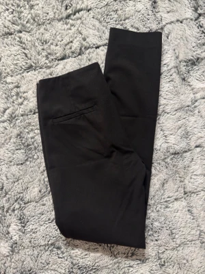 Flippa K kostymbyxor, xs  - Snygga svarta kostymbyxor med rak passform och minimalistisk design. Byxorna har en diskret bakficka och är tillverkade i ett slätt tyg som ger en stilren look. Perfekta för dig som vill ha en clean och klassisk stil.