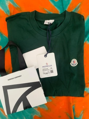Grön t-shirt från Moncler - Mörkgrön t-shirt från Moncler med rund halsringning och Moncler-logga broderad på bröstet. Tillverkad i mjuk bomull och har en klassisk passform. Perfekt för dig som gillar stilrena och exklusiva plagg.