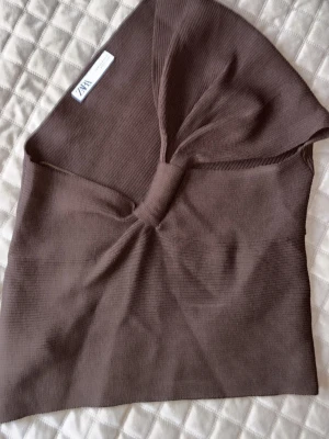 Brun ribbad tubtopp från Zara - Säljer en brun ribbad tubtopp från Zara i storlek M. Toppen har en snygg twistdetalj framtill och är axelbandslös, vilket ger en trendig och clean look. Perfekt att styla med jeans eller kjol för en cool vibe. Den är i nytt skick.