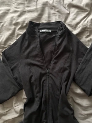 Svart jumpsuit från FB Sister - Säljer en svart jumpsuit från FB Sister i storlek XS. Den har lång ärm och dragkedja framtill som gör den enkel att ta på. Materialet är mjukt och stretchigt, perfekt för en chill och snygg look.