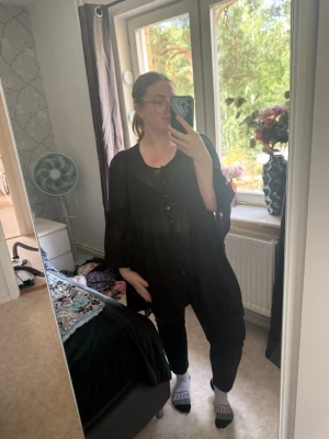 Svart oversize blus med knappar - Säljer en svart, luftig och oversize blus med knappar framtill. Blusen har långa, vida ärmar och en avslappnad passform som ger en cool och trendig look. Perfekt att styla med jeans eller leggings för en chill vibe. Storlek M. Men Zizzi storlek är storlek och denna är mer en XL. Mycket fint skick, jag hittar inga synliga anmärkningar eller defekter.  