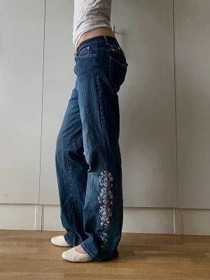 Vintage lågmidjade jeans med brodering - Mörkblå lowrise vintage denim jeans. Funkar för flera storlekar beroende på hur baggy man vill ha dem. Jag har strl 38 och är 176cm lång. Brodering längst ena benet och baksidan. Fungerande fickor fram och bak. 