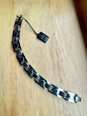 Stilrent länkat armband i rostfritt stål ca 20 cm - Snyggt armband i rostfritt stål med geometriska länkar och diskreta mönster. Armbandet har en modern design med rektangulära och fyrkantiga former, och en liten tagg där det står 'Italy'. Acane Rezetti design. Perfekt accessoar för att lyfta din outfit. Längd ca 20 cm och 13 mm brett Helt nytt
