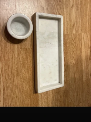 Vitt marmorfat och skål  - Säljer ett set med ett rektangulärt fat och en rund skål i vit marmor. Perfekt för att förvara småsaker, smycken eller använda som dekoration. Båda delarna har en stilren och minimalistisk design som passar in i de flesta hem.