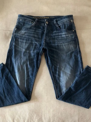 Blåa jeans med snygg tvätt - Säljer ett par mörkblå jeans med raka ben och snygga detaljer på bakfickorna, jeansen har en riktigt snygg tvätt med en riktigt najs pass form, passformen är straight och modellen heter ”tapered mike”. Jeansen är köpta i butik från jack&jones och dom är i riktigt fint skick, skriv för fler frågor!