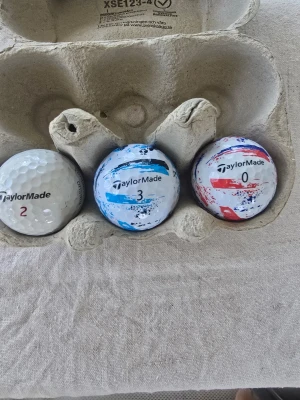 TaylorMade golfbollar med tryck - Tre golfbollar från TaylorMade, en vit med svart och röd text, en vit med blått mönster och en vit med rött och blått mönster. En boll har trycket 'anders effort ventilation ab onsala'. Perfekt för golfentusiasten som vill sticka ut på banan. Alla är tvättade men kan såklart finnas lite små skit kvar.  Kontakta om du tex bara vill ha två eller en så löser jag.