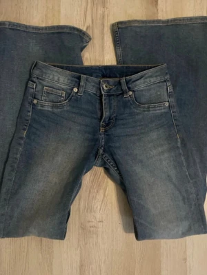 Blå bootcut jeans med fem fickor - Snygga blå jeans med klassisk femficksdesign och bootcut ben. Jeansen har en lätt tvättad look med subtila slitningar framtill och bakfickor utan dekorationer. Tillverkade i denim med normal midja och knappgylf. Perfekta för en avslappnad och trendig stil.