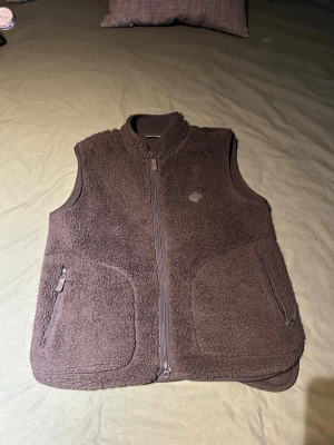 J.Lindeberg fleece väst - Mysig svart fleeceväst med hel dragkedja framtill och två stora fickor med dragkedja. Västen har en hög krage och är tillverkad i ett fluffigt material som håller värmen. Perfekt för lager-på-lager och chill dagar.