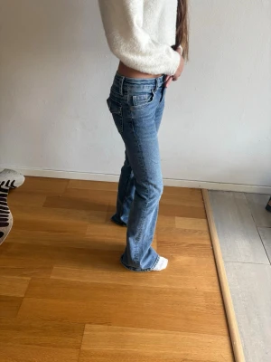Blå bootcut jeans med låg midja - Säljer ett par blå bootcut jeans med låg midja och klassiska fem fickor. Jeansen har en snygg tvätt och utsvängda ben som ger en retrovibe. Perfekta för dig som gillar en avslappnad men trendig stil.