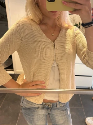 Beige stickad kofta med 3/4-ärm - Söt beige stickad kofta med 3/4-ärm och öppen framtill. Koftan har en enkel, rak passform och är tillverkad i ett mjukt, tunt material som passar perfekt till lager på lager. Enkel att matcha med olika outfits. 