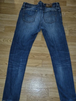 Blå raka jeans med slitningar - Säljer ett par klassiska blå jeans med raka ben och snygga slitningar. Jeansen har en tvättad look med ljusare partier på låren och knäna. Materialet är denim, vilket ger en skön och avslappnad känsla. Perfekta för en casual stil. 688 comfort jeans