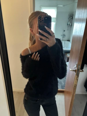 Svart fluffig off shoulder stickad tröja - Mysig svart stickad tröja med fluffig textur och off shoulder-modell. Tröjan har långa ärmar och en avslappnad passform som ger en trendig och bekväm look. Perfekt att styla med jeans för en cool vardagsstil.