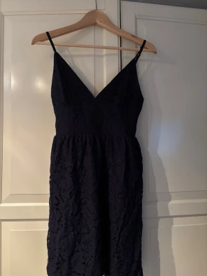Marinblå spetsklänning från New Eve - Snygg marinblå kort klänning från New Eve med spetsdetaljer och smala axelband. Klänningen har v-ringning och dragkedja i sidan. Perfekt för dig som vill ha en elegant look med en feminin touch.