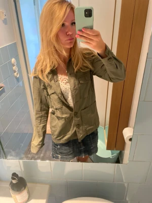 Olivgrön utilityjacka med fickor - Snygg olivgrön utilityjacka med fyra stora fickor framtill och knäppning med knappar. Jackan har en rak passform och är tillverkad i bomull, perfekt för lager på lager under vår och höst.