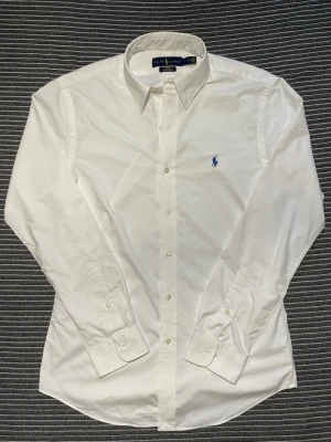 Vit Ralph Lauren skjorta - Mycket fet skjorta från Ralph Lauren i S Slim fit, vit med blå broderad logga | Nypris: ca 1900kr | Skjortan är allmänt i toppskick förutom ett pyttelitet hål (se sista bild), därav det bra priset! | Tveka inte på att höra av dig om du har funderingar!🙌