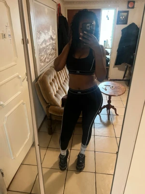 Svart träningsset från Alo - Säljer ett svart träningsset från Alo med sport-bh och höga tights. Setet har vita kontrastsömmar och logga på både bh och tights. Perfekt för gymmet eller löpning. Materialet är stretchigt och sitter tight mot kroppen.