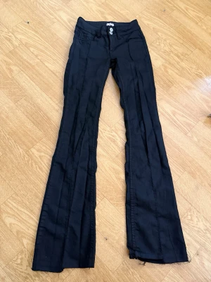 Svarta bootcut jeans från Nelly - Snygga svarta jeans från Nelly med bootcut-modell och dubbla knappar i midjan. Jeansen har klassiska fickor fram och bak samt markerade sömmar längs benen. Dem är uppsprättade längst ner(Se bild)