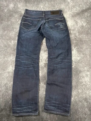 Mörkblå G-Star-jeans för herrar i storlek W32 L34 - Djup indigotvätt, lätt slitage och fint linjeformat slitage. Även lite distressing.  Skick: 9,5/10  Midja: 42 cm Benslut: 19 cm Lår: 31 cm Totallängd: 110 cm Måtten finns även på bilderna  Skickas inom ett dygn Spara på priset och frakten genom att sätta ihop ett paket! 5-118