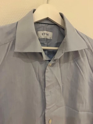 Ljusblå skjorta från Eton slim fit - Säljer en klassisk ljusblå skjorta från Eton i slim fit-modell. Skjortan har lång ärm, knappar framtill och en stilren krage. Perfekt för dig som gillar en clean och tidlös look.