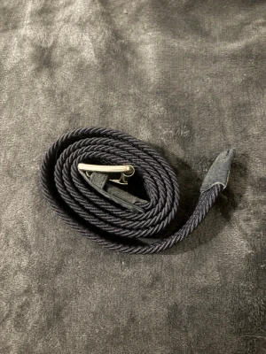 Svart flätat bälte med silverfärgat spänne - Snyggt svart flätat bälte med ett stilrent silverfärgat spänne. Bältet har detaljer i mocka vid ändarna och passar perfekt till jeans eller byxor för en clean look.