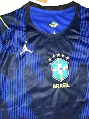 Blå Brasilien fotbollströja Dri-FIT - Snygg blå Brasilien fotbollströja från Jordan med Dri-FIT-material. Tröjan har gula detaljer, CBF-emblem och fyra stjärnor på bröstet. Perfekt för träning eller match, med modern passform och ventilerande tyg.