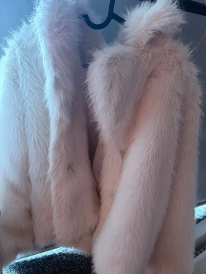 Vit fluffig pälsjacka - Supersnygg vit pälsjacka i fuskpäls med mjuk och fluffig känsla. Jackan har en klassisk rak passform och bred krage som ger en trendig look. Perfekt för att hålla värmen under kalla dagar och ger en lyxig vibe till din outfit. Den har en lila fläck vid fickan som oftast inte syns men är där. Har inte försökt få bort då jag inte vet hur men fläcken är från spray paint. 