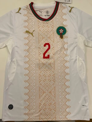 Hakimi Marocko 2026 Vm bortatröja - Fotbollströja i helt nytt och oanvänt skick med tag kvar. Detaljrik design och bekvämt material som passar både till match och vardag. Detta är en inofficiell version av modellen. Storlek M