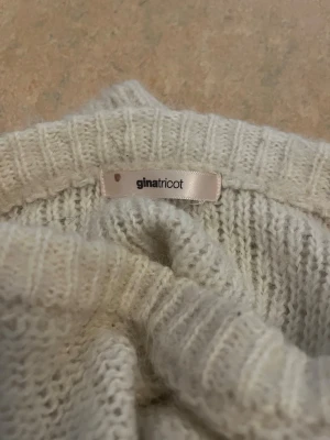 Vit stickad tröja från Gina Tricot - Mysig vit stickad tröja från Gina Tricot med kabelstickat mönster på framsidan. Tröjan har långa ärmar, ribbade muddar och en något kortare, boxig passform. Perfekt för lager på lager under kyliga dagar.