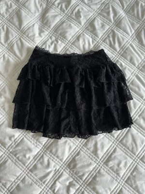 Svart spetskjol med volanger - Säljer en svart kortkjol i spets med flera lager volanger. Elastisk midja för skön passform och snygg struktur. Inbyggda shorts.