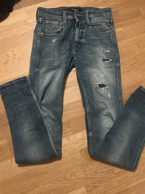 Replay jeans - Snygga blå jeans med slitningar och hål på framsidan. Jeansen har fem fickor, normal midja och klassisk passform. Färgen är tvättad denim med ljusare partier och detaljerade sömmar på bakfickorna. Perfekta för en avslappnad och trendig look.