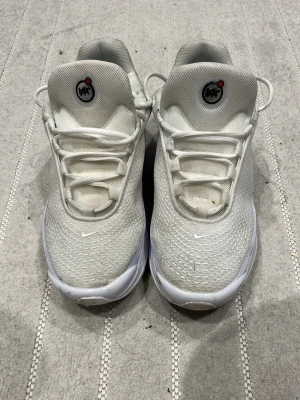 Vita Nike Air Max sneakers - Säljer ett par vita Nike Air Max sneakers med mesh-överdel och unika luftbubblor i sulan. Skorna har en sportig design med diskreta grå detaljer och små Nike-loggor på sidan och tungan. Perfekta för dig som gillar en clean och modern look.