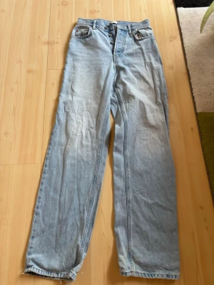 Ljusblå raka jeans med hög midja - Säljer ett par ljusblå jeans med raka ben och hög midja. Jeansen har klassisk femficksdesign, knäppning fram och är tillverkade i denim. 