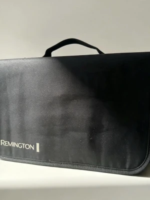 Remington stylingverktyg med tillbehör - Snyggt svart stylingverktyg från Remington i praktisk väska. Setet innehåller flera utbytbara borsthuvuden och munstycken för olika hårstylingar. Perfekt för dig som vill fixa håret hemma med proffsiga resultat. Allt ligger samlat i en smidig, svart tygväska med handtag.