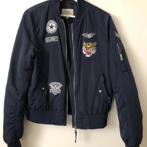 Bomberjacka  - Marinblå bomberjacka i märket ”Softy Outerwear” med olika tygmärken. Storlek XL men är snarare en L. Är i lite tjockare material och därmed perfekt att ha på hösten och våren.