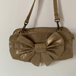Liten väska med en rosett i färgen guld  - Liten väska i färgen guld 
