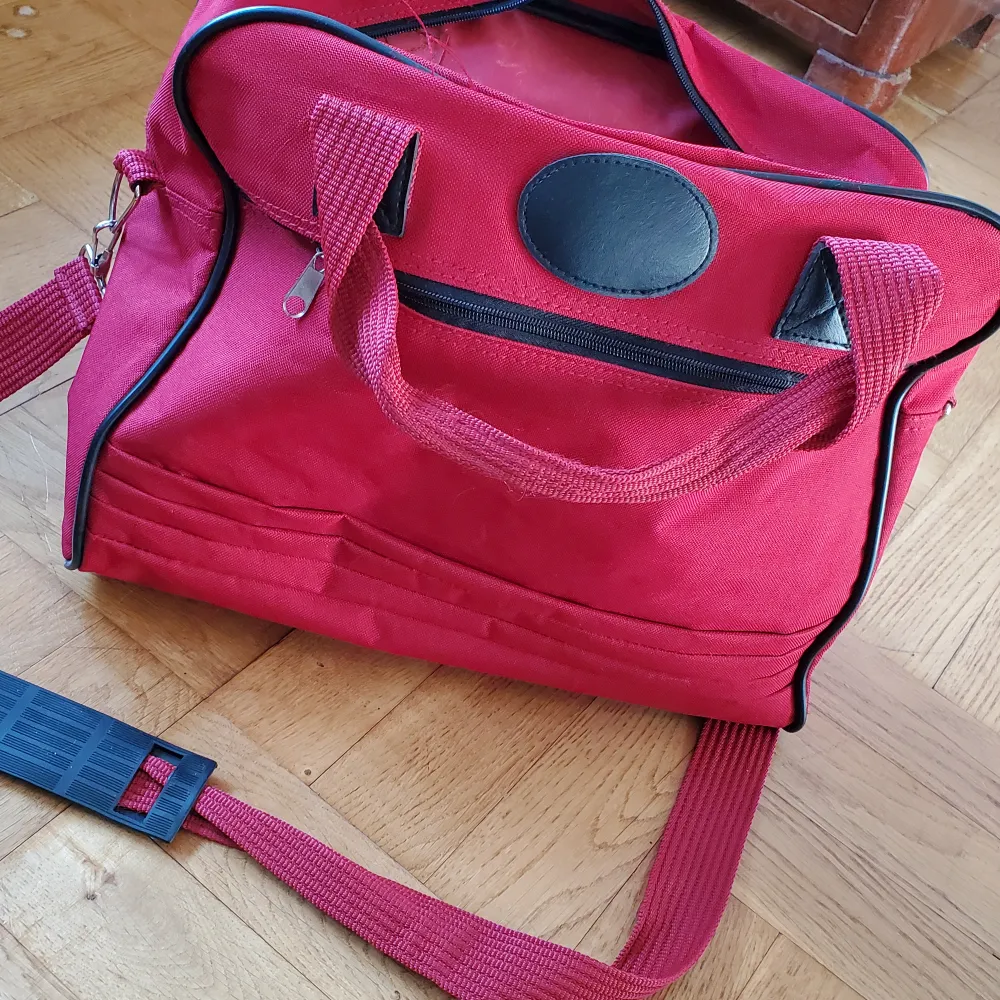 Röd väska med avtagbar axelrem, mindre ficka fram med dragkedja. . Väskor.