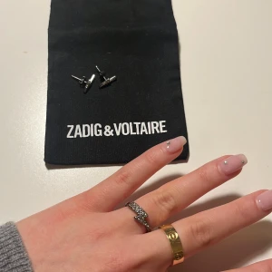 Zadig & Voltaire smycken - En ring och örhängen från Zadig & Voltaire. Pyttelite stavd färg på den ringen (syns knappt). Tre stenar borta från örhängena. Båda för 500kr eller örhängena för 250kr och ringen 400kr.