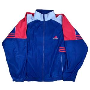 Vintage Adidas Trackjacket i storlek XL. I blå, röd och grå färg. Den är i bra skick utan några defekter.