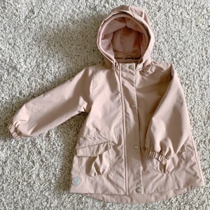 Wheat Jacket  - A shaped technical jacket in waterproof and breathable fabric.  - Adjustable drawstring at the waist  - Detachable hood  - Standard 100 by OEKO-TEX - Color: Dusty pink  - Material: Recycled Nylon  - Condition: 80% looking new 