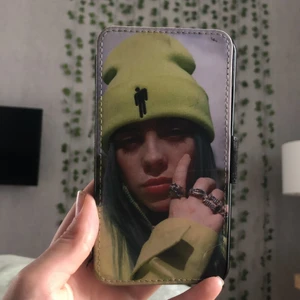 Billie Eilish mobilskal  - Ett plånboks liknande mobilfodral med billie Eilish på. Jätte fint skick förutom en repa fram som man ser på bild 3.