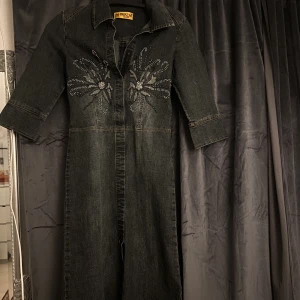 Jeansklänning - Jeansklännikng med trekvarts ärmar och strass. Klänningen går precis över knäna och framhäver figuren på bästa sätt. Det finns knappar så att man kan justera hur öppen eller stängd den ska vara 🫶🏻🥰
