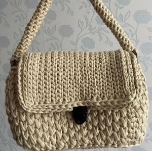 Handväska - Beige väska med guld och mattsvarta detaljer. Väskan har guldiga väskfötter.  längd: 24cm höjd: 17cm ( inkl. handtag: 30.5 cm) bredd: 9cm Material: trikå/bomullsgarn Pris: 1000kr+porto OBS!! Katter finns i hemmet