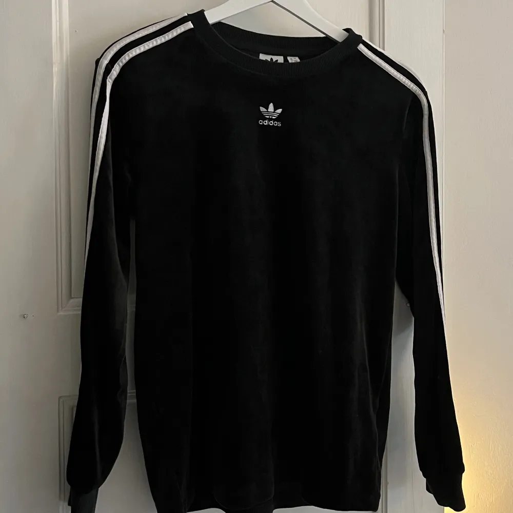 En otroligt fin retro adidas -tröja i svart med ränder på ärmarna och loggan i mitten på bröstet. Detta är det lenaste plagget jag äger, materialet är som velvet 💘 Bara använd ett fåtal gånger så otroligt bra skick!. Toppar.