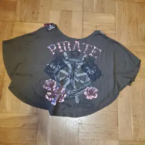 Köpt på Disneyland, Kalifornien, officiell merch från Pirates Of The Caribbean-serien. Tryck av roder, nyckel, piratflaggor och rosa blommor samt detaljer på axlarna. Rund form nedtill. Okej att komma med bud. Katt i hemmet. 