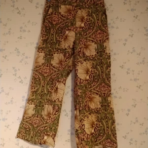 Blommiga byxor - Byxor med vackert mönster av blommor o blad. Har dragkedja,fickor i sidorna och hällor för bälte. 89% lyocell 11% polyester. OBS jag har lagt upp benen, jag är 155 cm och de slutar lite över mina anklar. 