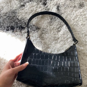 Svart glansig väska  - Plast, oanvänd. Får plats med telefon smink plånbok 