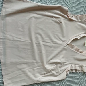 Linne - Ärmlös topp. Volang runt hals och ärm. Ljus rosa, inte genomskinlig. 