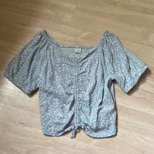 En blå topp med blommor. - En blå och vit topp med en stretchiga baksida även en rosett på framsidan.