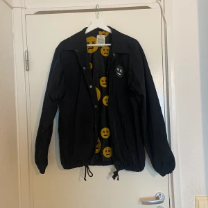 Blå regnjacka med smile ansikten  - En regnajacka med storlek M, köpt på carlings. Lite oversize, så kan passa M/L/XL. Köptes för några år sen så ser använd ut. 